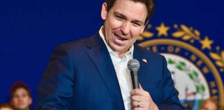 A man in a blue suit speaking into a microphone at a public event