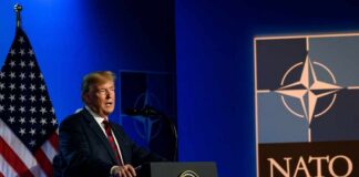Trump’s Warning: NATO’s Future in Jeopardy A man speaking at a podium with a NATO logo and an American flag in the background
