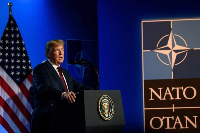 A man speaking at a podium with a NATO logo and an American flag in the background