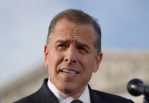 Hunter’s Legal Woes Deepen Amid Cage Match Chaos Man in a suit speaking at an outdoor event with a microphone