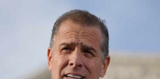 Man in a suit speaking at an outdoor event with a microphone