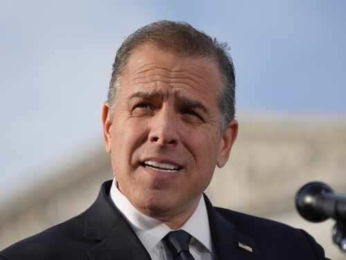 Man in a suit speaking at an outdoor event with a microphone