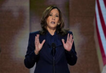 A woman in formal attire delivering a speech at a podium with an American flag in the background