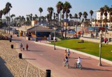 Nation’s Biggest Exodus Hits Los Angeles People walking and biking along a beach promenade with palm trees
