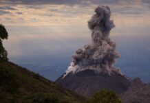 Volcano erupting with a large plume of smoke against a cloudy sky