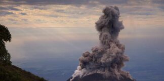 Volcano erupting with a large plume of smoke against a cloudy sky