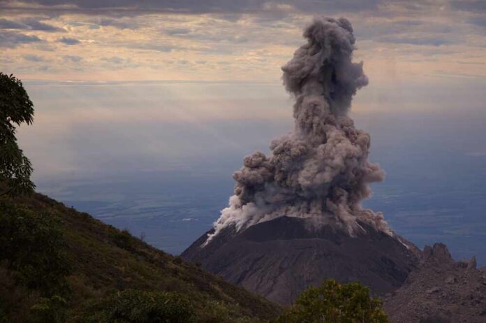 Volcano erupting with a large plume of smoke against a cloudy sky