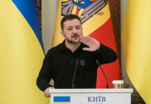 Ukrainian leader speaking at a podium with national flags in the background