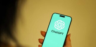 A person holding a smartphone displaying the ChatGPT logo on a teal background
