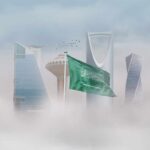 Saudi Arabian flag in front of a modern city skyline shrouded in fog