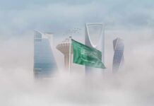 Saudi Arabian flag in front of a modern city skyline shrouded in fog