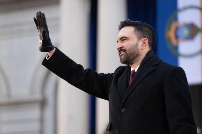 A man in a black coat and gloves waving at an outdoor event