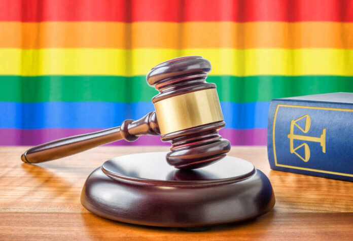 A wooden gavel on a table with a rainbow flag in the background