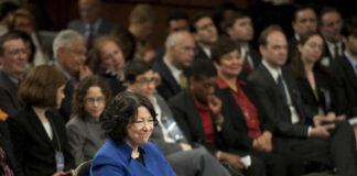 A woman in a blue suit smiling at a Senate confirmation hearing with an audience in the background