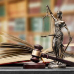 A gavel and a statue of Lady Justice beside an open law book