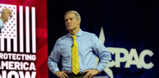 Political CHAOS Shakes Supreme Court Debate A man in a blue shirt and yellow tie stands on stage at a political conference