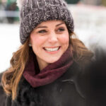 A woman smiling warmly while wearing a knitted hat and scarf in a winter setting