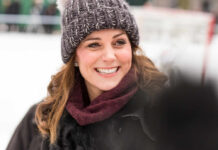 A woman smiling warmly while wearing a knitted hat and scarf in a winter setting