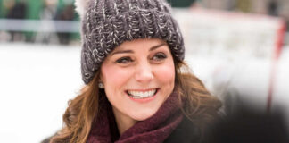 A woman smiling warmly while wearing a knitted hat and scarf in a winter setting