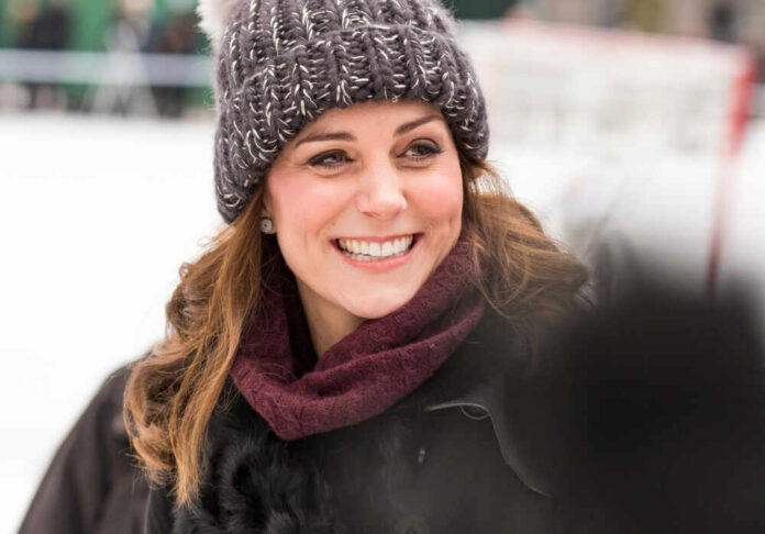 A woman smiling warmly while wearing a knitted hat and scarf in a winter setting