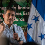 A speaker passionately addressing an audience with the Honduran flag in the background
