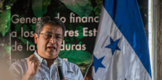 A speaker passionately addressing an audience with the Honduran flag in the background