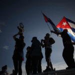 Silhouetted figures celebrating with a trophy and Cuban flags against a sunset sky