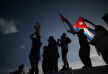 Silhouetted figures celebrating with a trophy and Cuban flags against a sunset sky