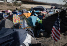 A crowded tent encampment near a border area with an American flag visible