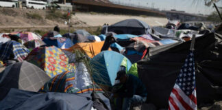 A crowded tent encampment near a border area with an American flag visible