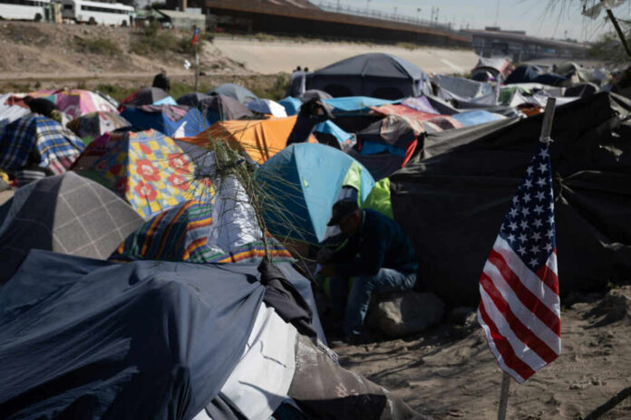 A crowded tent encampment near a border area with an American flag visible