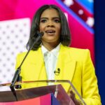 A woman in a bright yellow suit speaking at a podium during a conference