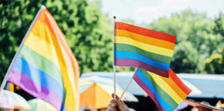 Mayor Hesitates As Advocates Demand Crisis A hand holding rainbow flags at a pride event with a crowd in the background