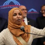A woman in a hijab passionately speaking at a podium during a public event