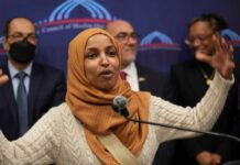A woman in a hijab passionately speaking at a podium during a public event