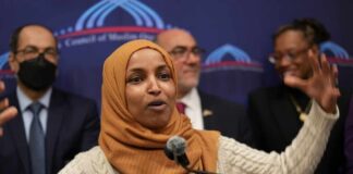 A woman in a hijab passionately speaking at a podium during a public event
