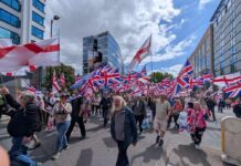 A large crowd of people marching with British flags in an urban area