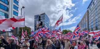 A large crowd of people marching with British flags in an urban area
