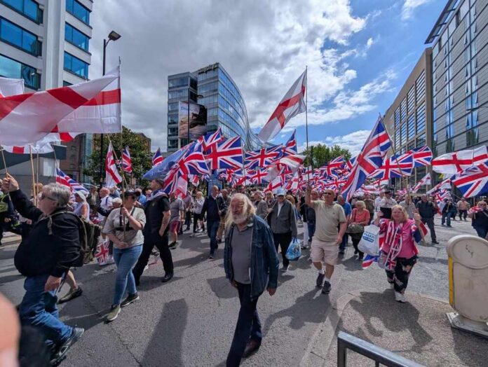 A large crowd of people marching with British flags in an urban area