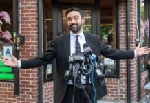 NYC’s $1.3M Shelter Blunder – Residents Rebel! Man in a suit speaking at a press conference with microphones in front of him