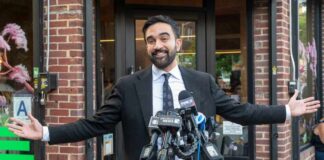 NYC’s $1.3M Shelter Blunder – Residents Rebel! Man in a suit speaking at a press conference with microphones in front of him