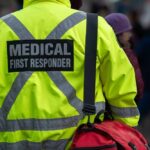 Medical first responder wearing a bright yellow jacket and carrying a red bag