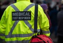Medical first responder wearing a bright yellow jacket and carrying a red bag