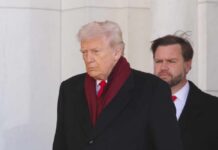 A political figure walking with a serious expression, wearing a dark coat and red scarf