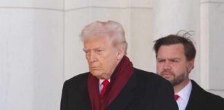 A political figure walking with a serious expression, wearing a dark coat and red scarf