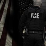 ICE agent standing in front of an American flag