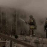Firefighters spray water into a smoke-filled structure
