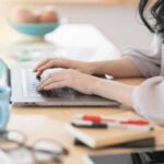 Person typing on a laptop at a home office desk with a coffee cup nearby
