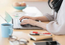 Four-Day Week Torches Office Waste Person typing on a laptop at a home office desk with a coffee cup nearby