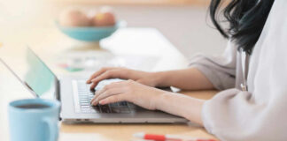 Person typing on a laptop at a home office desk with a coffee cup nearby